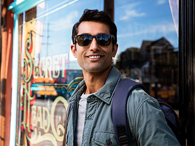 A man wearing sunglasses, standing outdoors with a backpack, smiling at the camera.